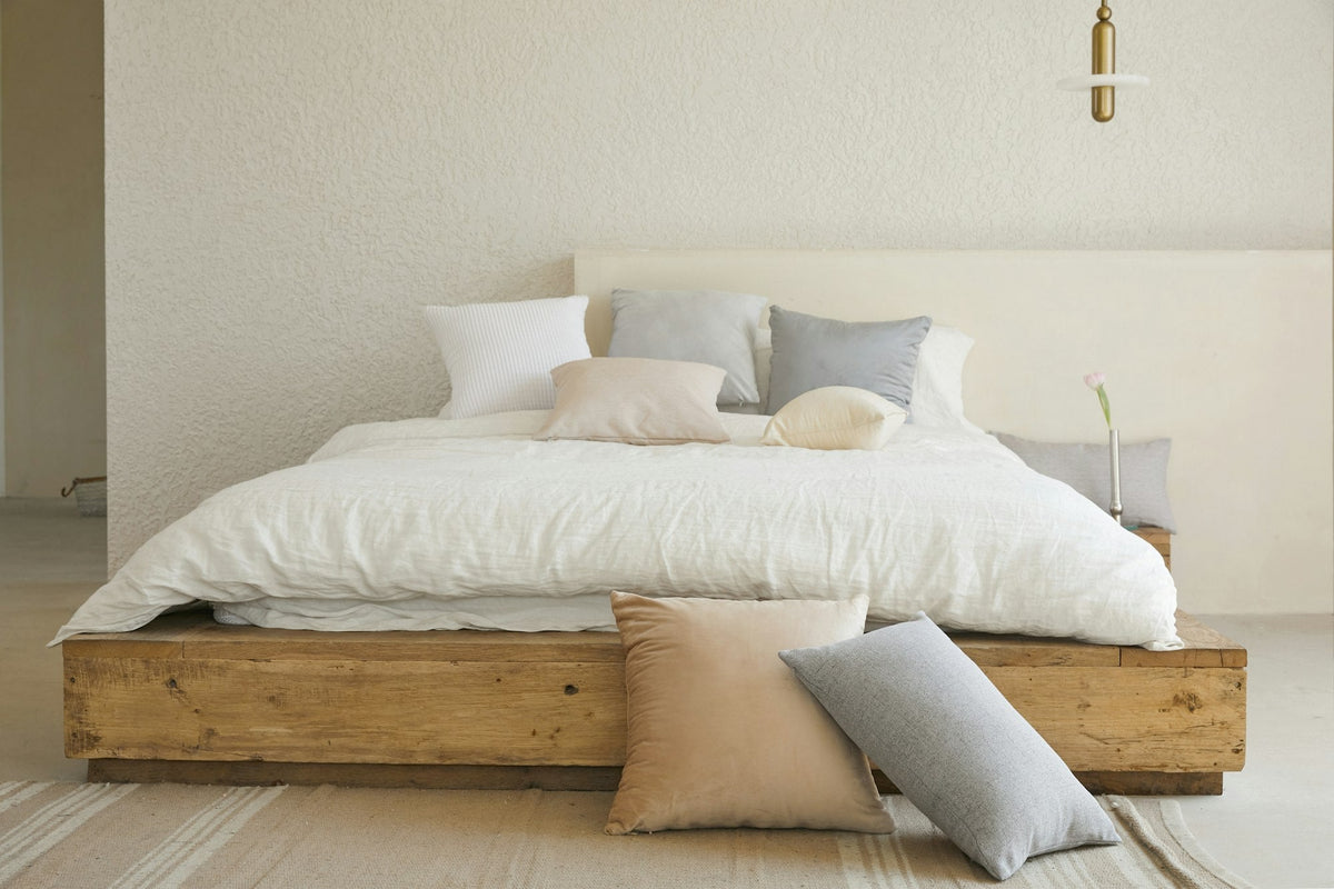 Opgemaakt bed met witte en grijze kussens op een houten bedframe